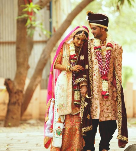 A joyful couple celebrates their traditional Indian wedding in vibrant outdoor attire.